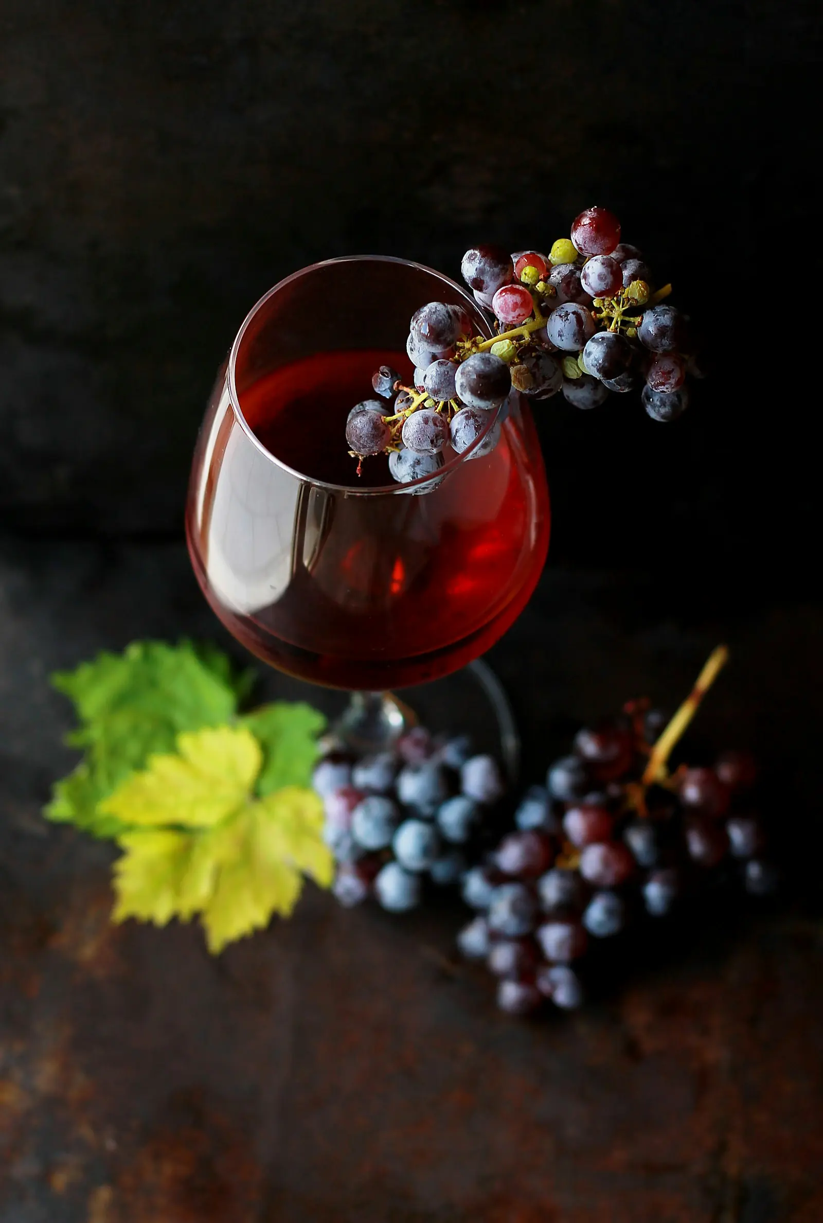 A glass of red wine beside a cluster of dark grapes on a dark table